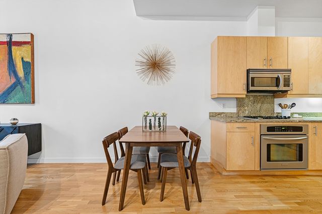 a kitchen with stainless steel appliances kitchen island granite countertop a dining table chairs and a refrigerator