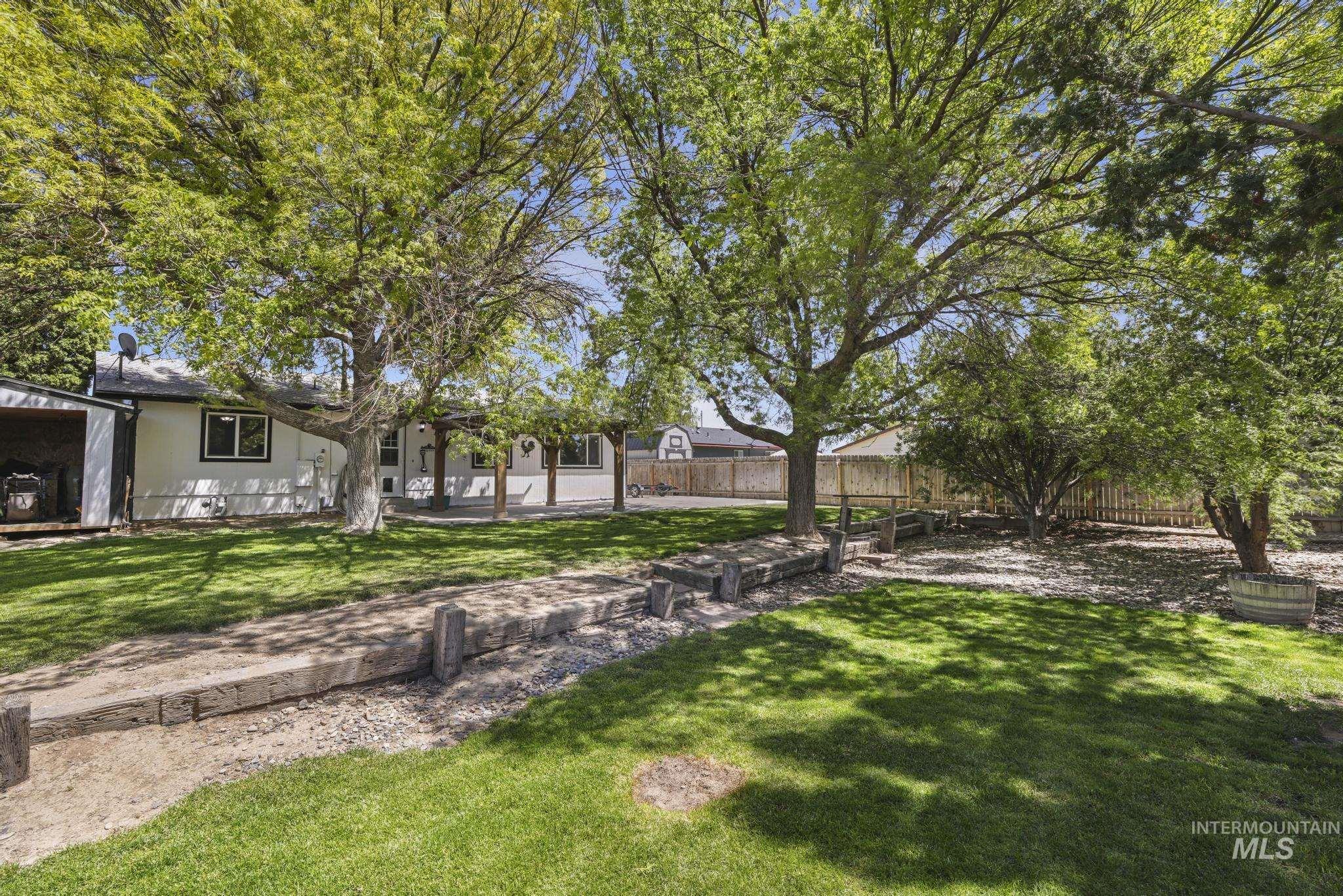 712 Locust Street Kimberly, ID 83341 - Photo 23 of 26 Expansive green lawn featuring a mature shade tree, a covered patio with exposed wood beams, and a detached storage shed with an open bay