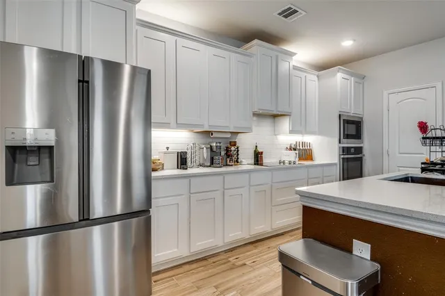 a kitchen with stainless steel appliances granite countertop a refrigerator a sink dishwasher a stove and white countertops with wooden floor