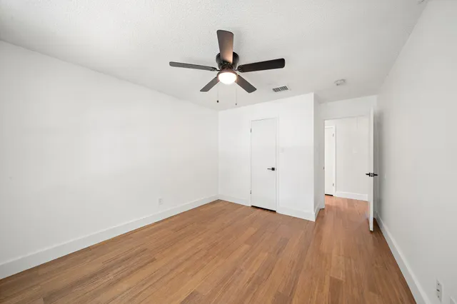 a view of empty room with wooden floor and fan