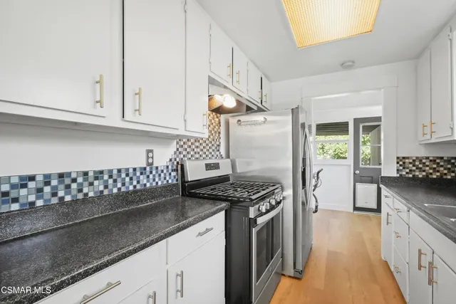 a kitchen with granite countertop a stove a sink dishwasher and white cabinets with wooden floor