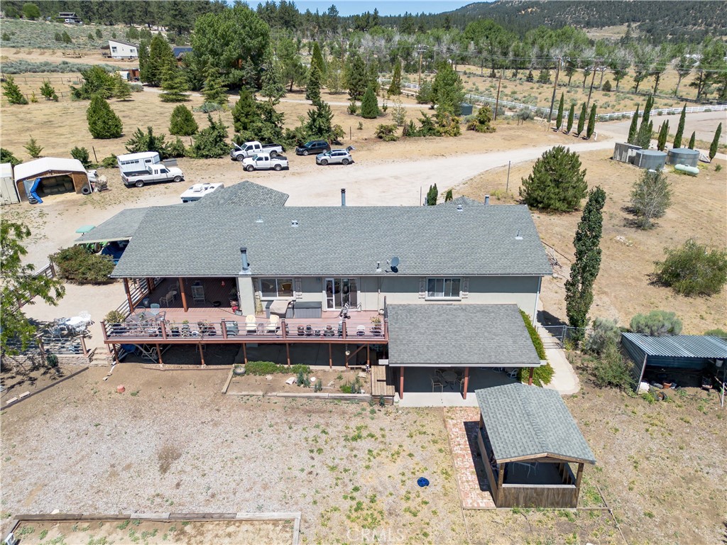 10960 Steinhoff Road Frazier Park, CA 93225 - Photo 6 of 46 An elevated aerial perspective capturing the rear profile of the home, showcasing the spacious multi-level deck, a detached covered shelter, and the surrounding terrain with mature trees and property parking in the background.