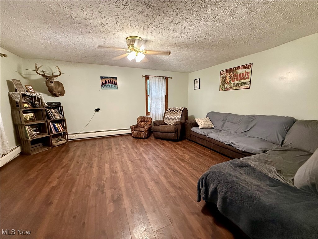 8195 Nichols Road Windham, OH 44288 - Photo 9 of 41 Living room featuring baseboard heating, ceiling fan, wood finished floors, and a textured ceiling