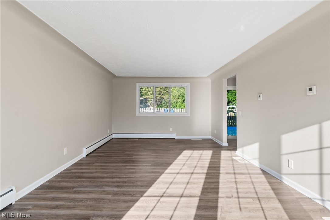Unfurnished room featuring a baseboard heating unit and hardwood / wood-style floors