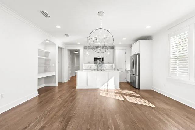 a large room with wooden floor a kitchen and windows