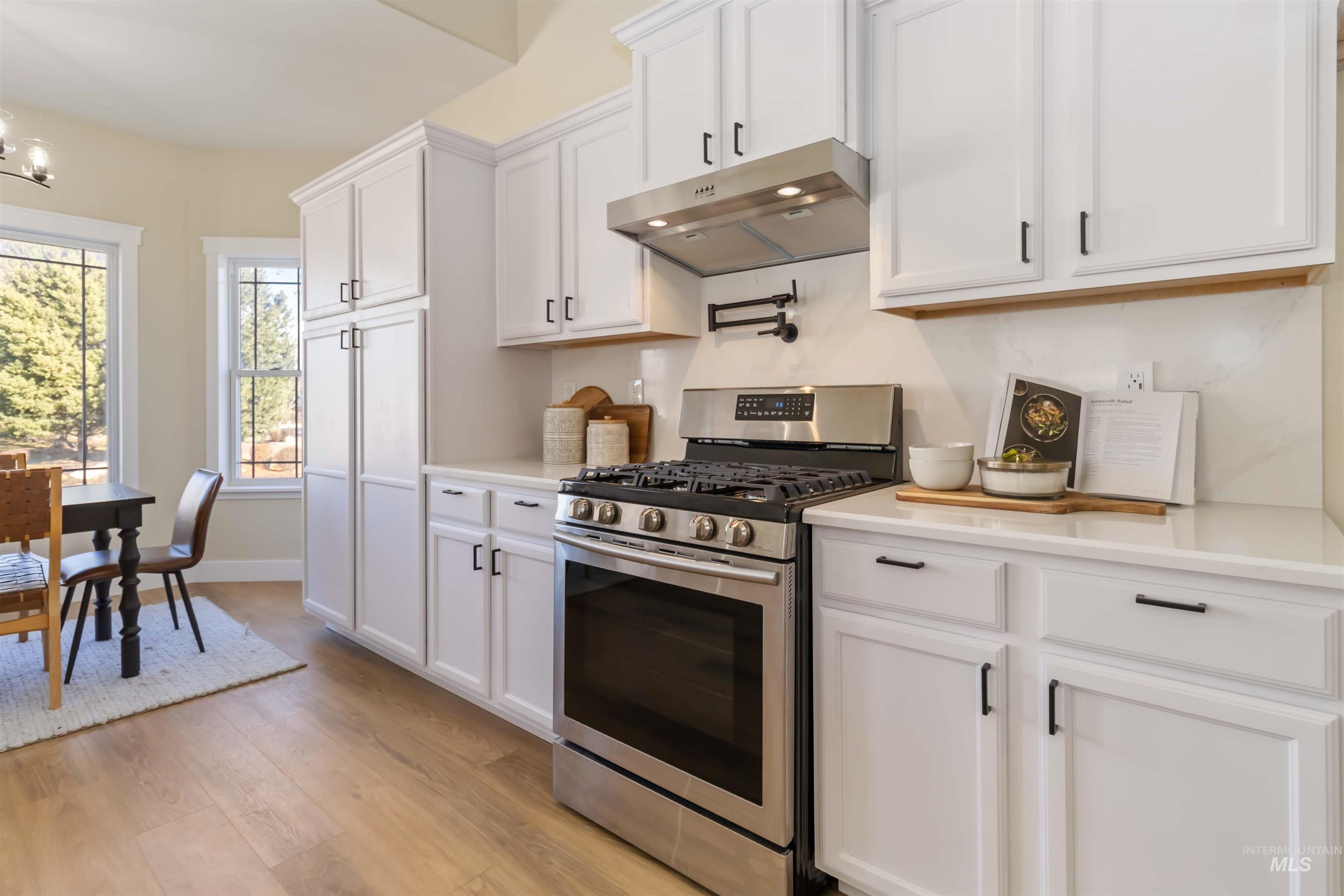 3201 Raintree Drive Nampa, ID 83686 - Photo 7 of 50 Kitchen with stainless steel gas range oven, under cabinet range hood, white cabinetry, and light wood finished floors