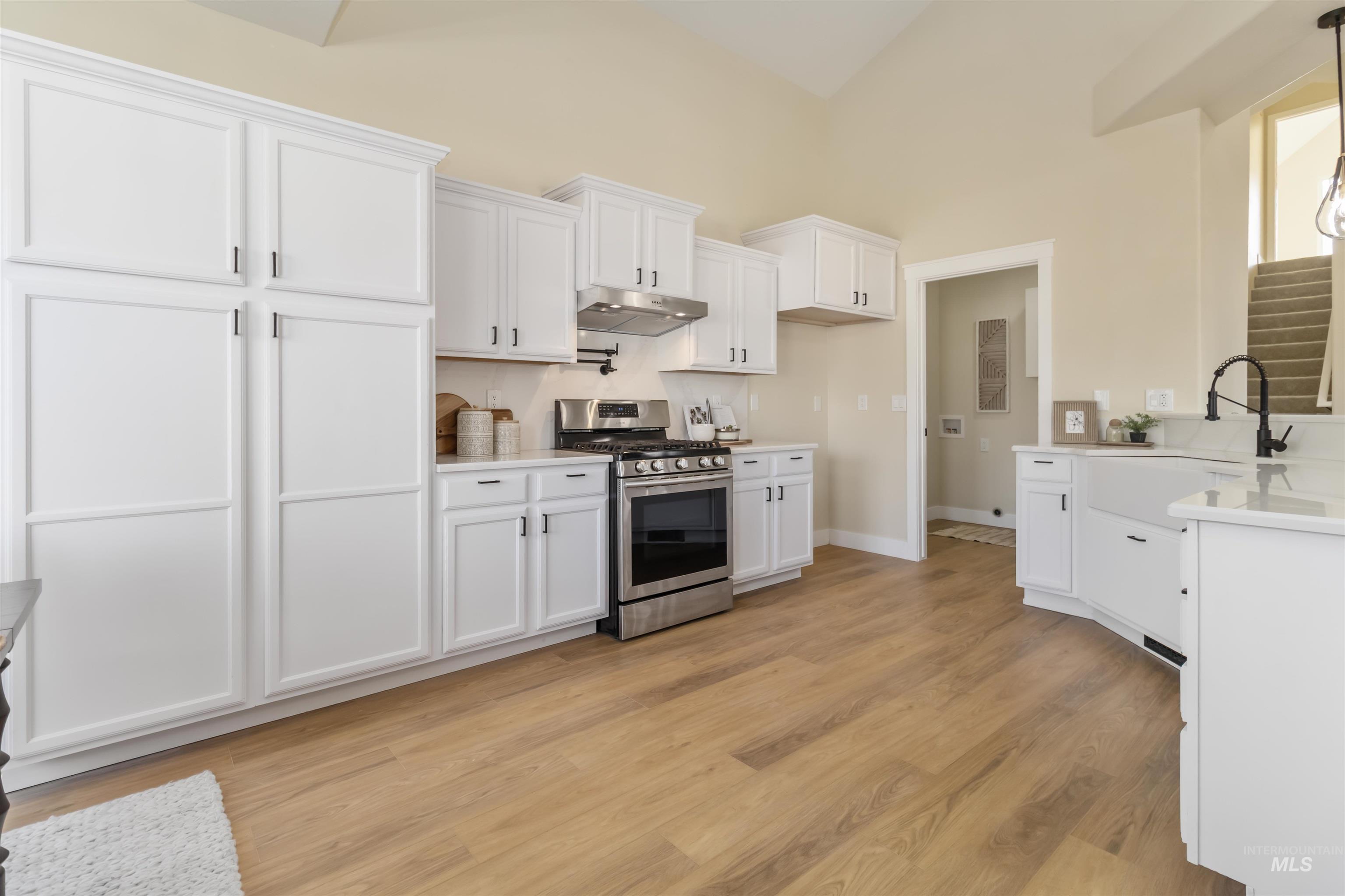 3201 Raintree Drive Nampa, ID 83686 - Photo 9 of 50 Kitchen featuring stainless steel gas stove, white cabinetry, under cabinet range hood, light stone counters, and high vaulted ceiling