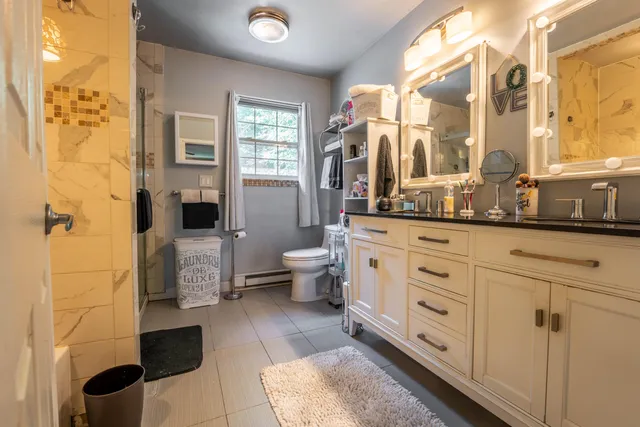 a spacious bathroom with a double vanity sink a toilet a mirror and shower