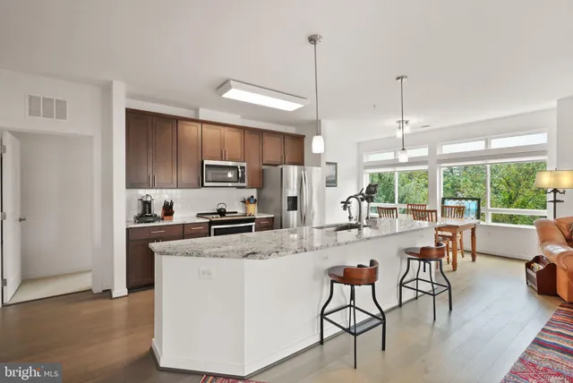 a kitchen with stainless steel appliances granite countertop a stove top oven a sink a dining table and chairs with wooden floor