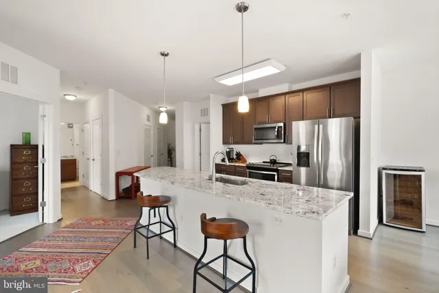 a kitchen with stainless steel appliances granite countertop a refrigerator a oven a sink a stove a dining table and chairs with wooden floor