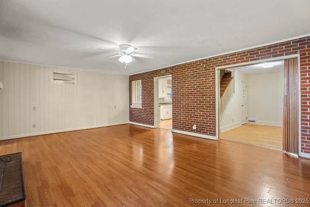 an empty room with wooden floor chandelier fan and windows