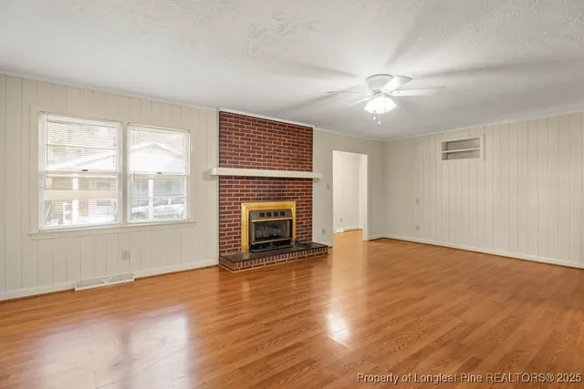 a view of an empty room with wooden floor fireplace and a window