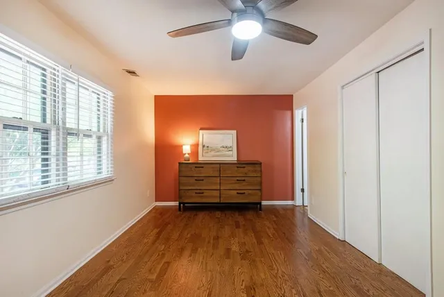 an empty room with wooden floor ceiling fan and windows