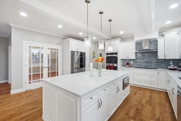 a large white kitchen with a large kitchen island white cabinetry and wooden floor