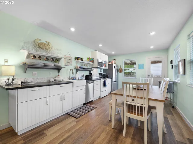 a kitchen with stainless steel appliances granite countertop a stove top oven a sink a dining table and chairs with wooden floor