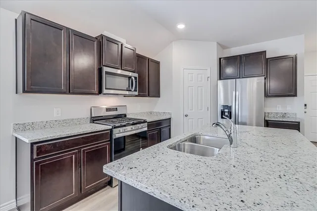 a large kitchen with stainless steel appliances a large counter top stove a sink dishwasher and a refrigerator with wooden floor