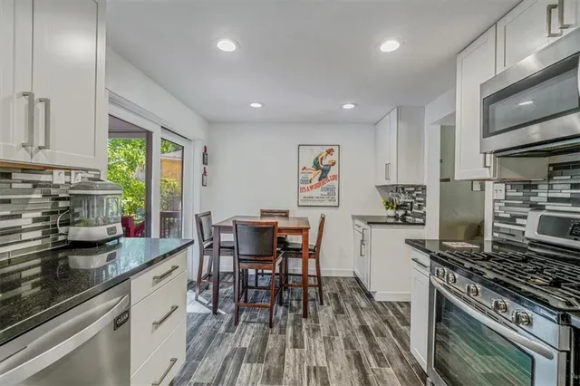 a kitchen with stainless steel appliances granite countertop a stove top oven a sink dishwasher a dining table and chairs with wooden floor