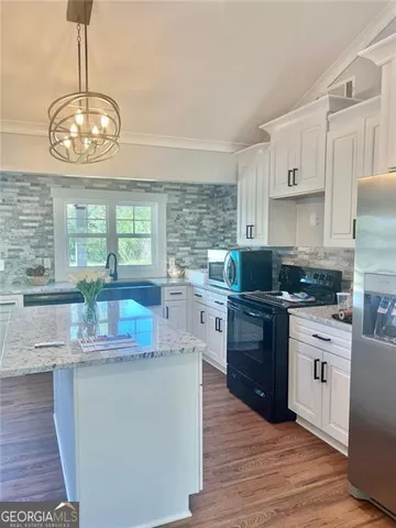 a kitchen with stainless steel appliances granite countertop a stove top oven a sink dishwasher a refrigerator and white cabinets with wooden floor