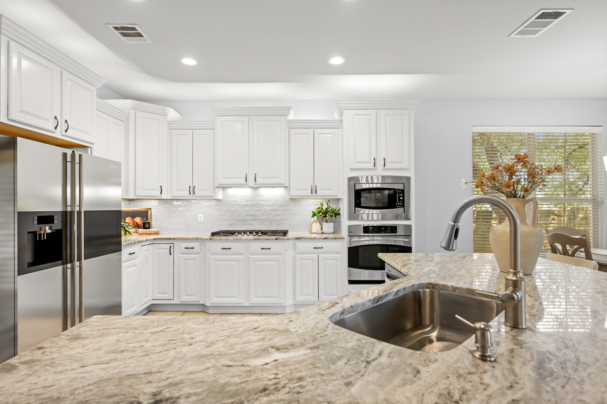 1023 Grassy Field Road Austin, TX 78737 - Photo 10 of 40 Kitchen featuring white cabinetry, built-in stainless steel appliances, a gas cooktop, a tile backsplash, and dolomitic marble countertops.