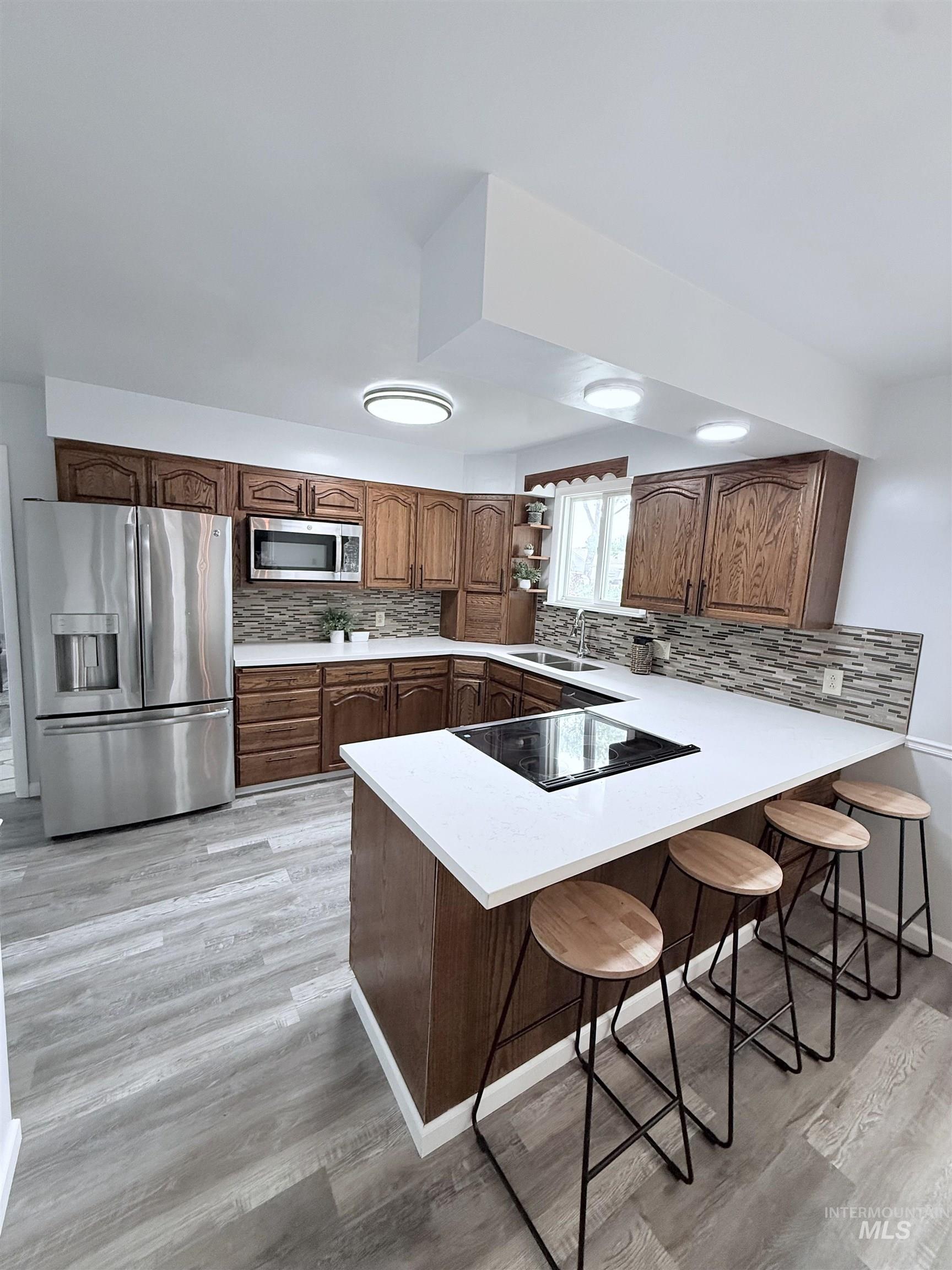 202 East Avenue Wendell, ID 83355 - Photo 5 of 24 Kitchen featuring appliances with stainless steel finishes, a peninsula, brown cabinetry, and a kitchen bar