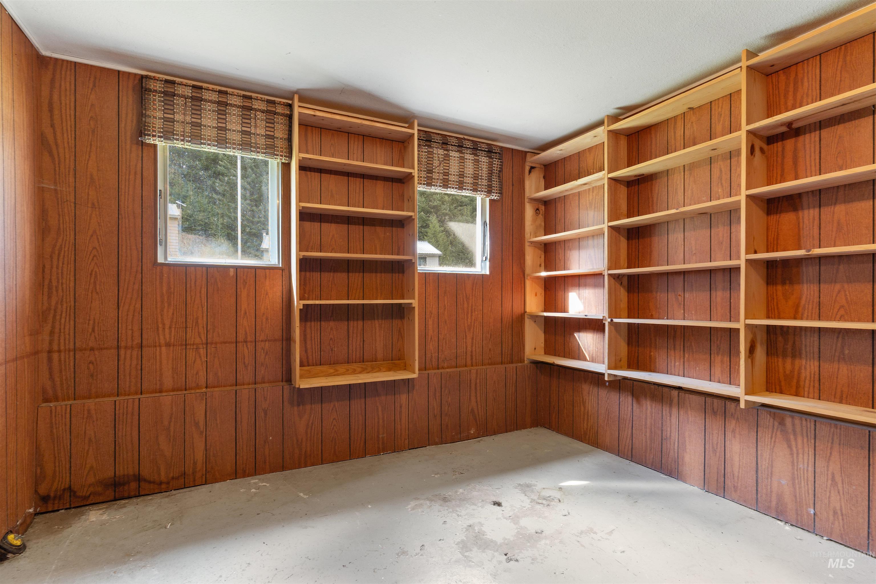145 Timberline Drive Pierce, ID 83546 - Photo 24 of 39 Room featuring wood paneling, multiple built-in shelving units, two windows with woven blinds, and a concrete floor
