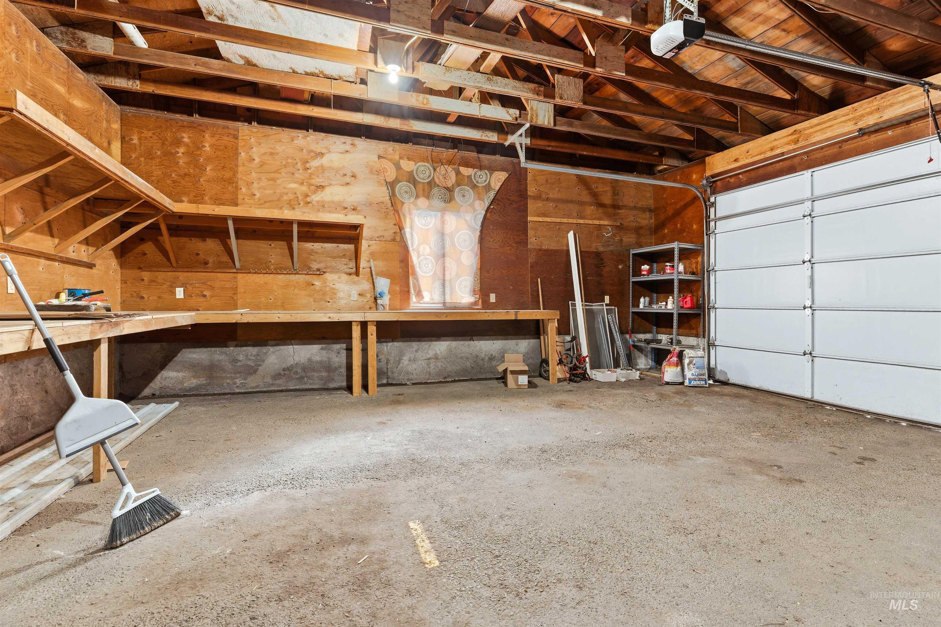 145 Timberline Drive Pierce, ID 83546 - Photo 25 of 39 Attached garage featuring an automatic overhead door, exposed wood beam ceiling, concrete flooring, and built-in plywood shelving and workbench