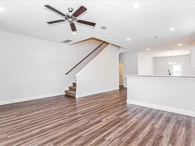 a view of an empty room with wooden floor and a ceiling fan