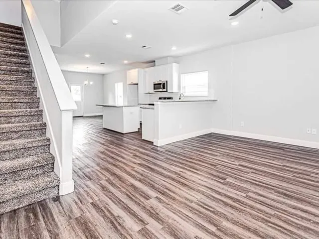 an empty room with wooden floor and kitchen view