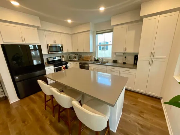 a kitchen with stainless steel appliances granite countertop a refrigerator a stove top oven a sink dishwasher and white cabinets with wooden floor