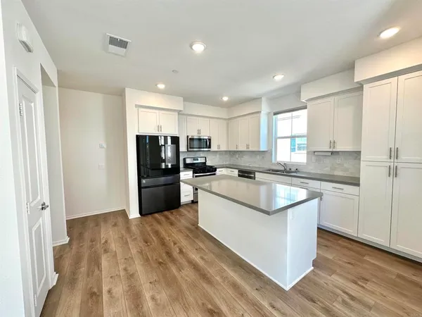 a kitchen with stainless steel appliances granite countertop a refrigerator a sink dishwasher a stove and white countertops with wooden floor