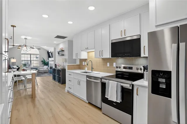 a kitchen with stainless steel appliances a stove a sink a refrigerator and white cabinets
