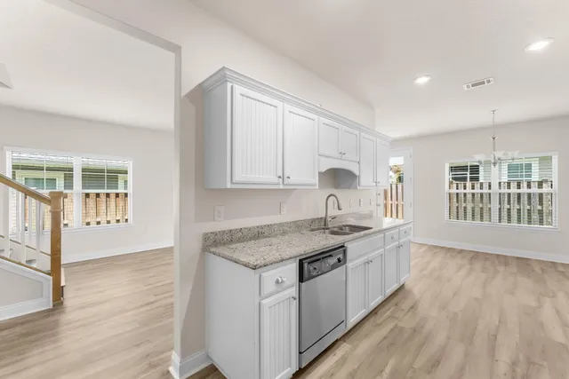 a kitchen with stainless steel appliances granite countertop a stove a sink and white cabinets with wooden floor