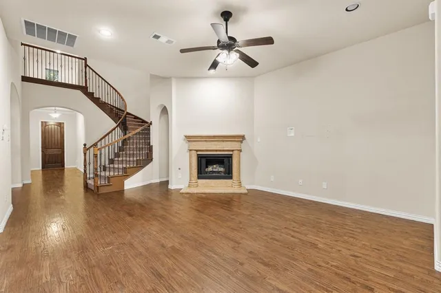 a view of an empty room with wooden floor a ceiling fan and a kitchen view