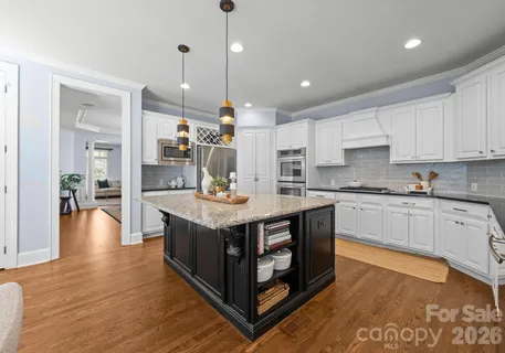 a kitchen with stainless steel appliances granite countertop a stove a sink a refrigerator and white cabinets with wooden floor