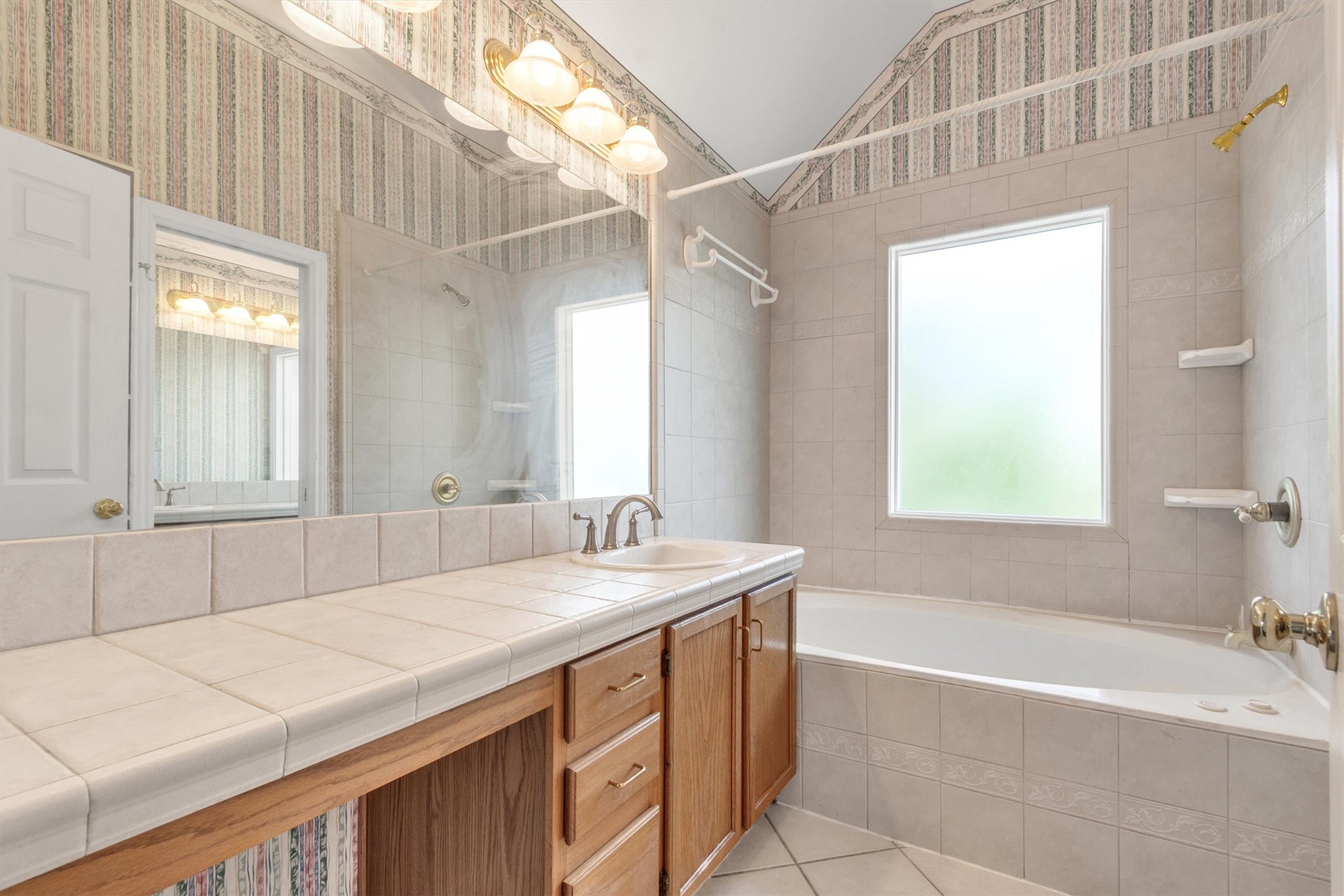 1207 Orlando Road Austin, TX 78733 - Photo 17 of 30 Bathroom featuring a full-width vanity mirror, tile countertop, wood-finish cabinetry, and a built-in bathtub with tiled surround