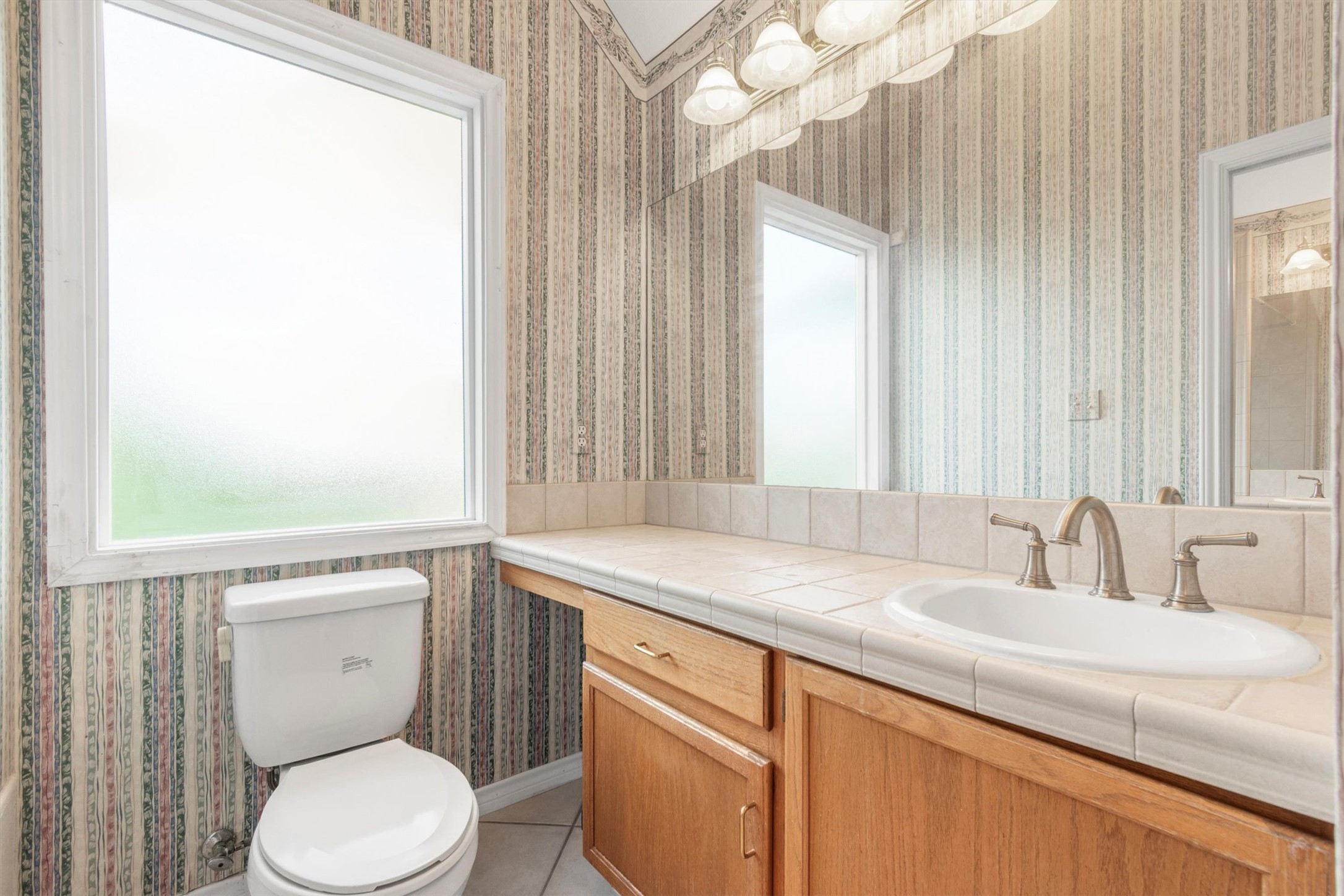 1207 Orlando Road Austin, TX 78733 - Photo 18 of 30 Bathroom featuring a large frosted window, tile-top vanity with an integrated sink, brushed nickel faucet, wood cabinetry, and overhead sconce lighting