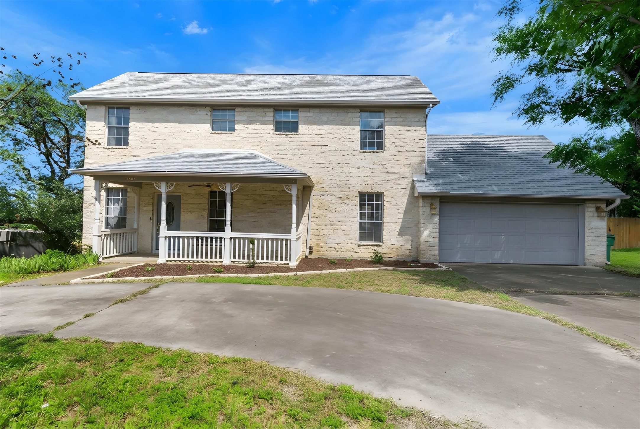 1207 Orlando Road Austin, TX 78733 - Photo 30 of 30 Stone exterior residence featuring a covered front porch with white railing, a two-car garage, and a paved driveway