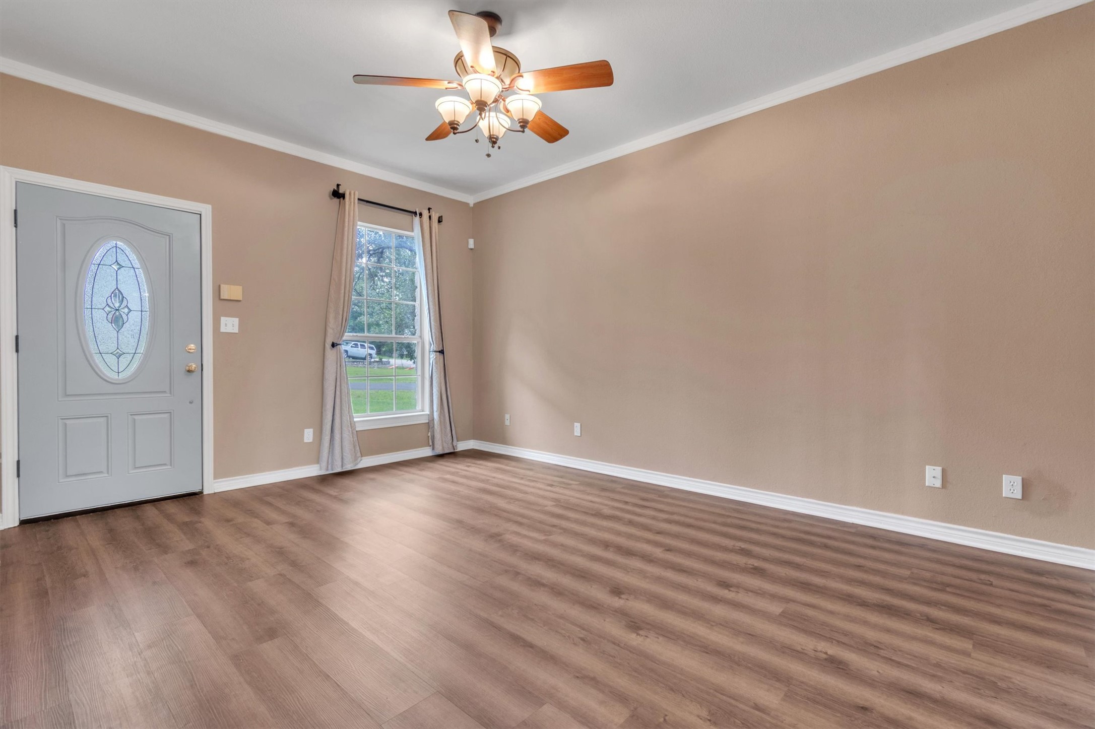 1207 Orlando Road Austin, TX 78733 - Photo 3 of 30 Spacious room featuring wood-finish flooring, a decorative front entry door with an oval stained-glass insert, a window with outdoor views, and a ceiling fan with integrated lighting