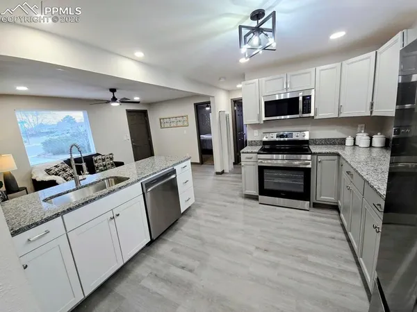 a large kitchen with stainless steel appliances granite countertop a stove top oven a sink dishwasher and a microwave with wooden floor