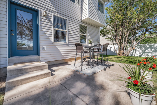 1147 West State Road Lehi, UT 84043 - Photo 28 of 31 Private concrete patio area featuring a vibrant blue glass-paneled door, white horizontal siding, a prominent shade tree, and a manicured lawn