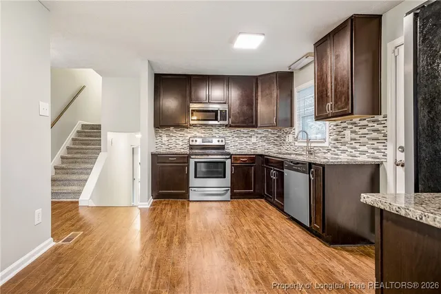a kitchen with stainless steel appliances granite countertop wooden floors and wooden cabinets