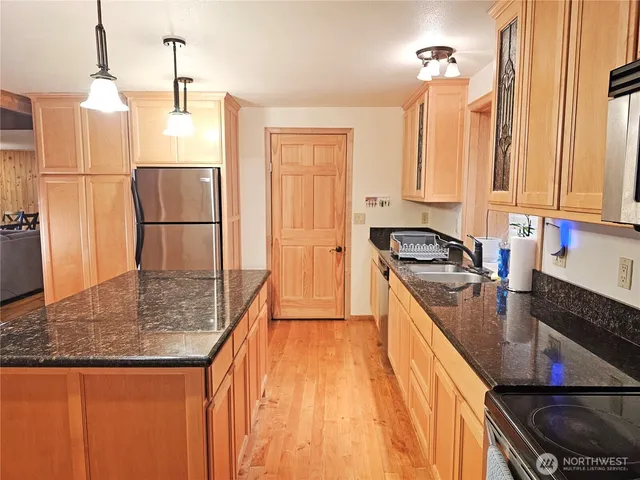 a kitchen with stainless steel appliances granite countertop a sink a stove a refrigerator a center island with wooden floor and cabinets