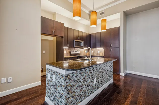 a kitchen with stainless steel appliances granite countertop a sink a microwave a refrigerator and wooden floor