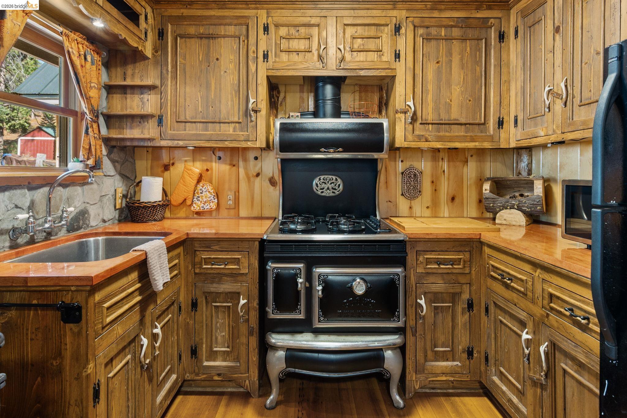 25972 Long Barn Road Long Barn, CA 95335 - Photo 9 of 36 Rustic kitchen featuring custom wood cabinetry with antler horned cabinet pulls, beautiful wood countertops, and a vintage-style range with an integrated oven
