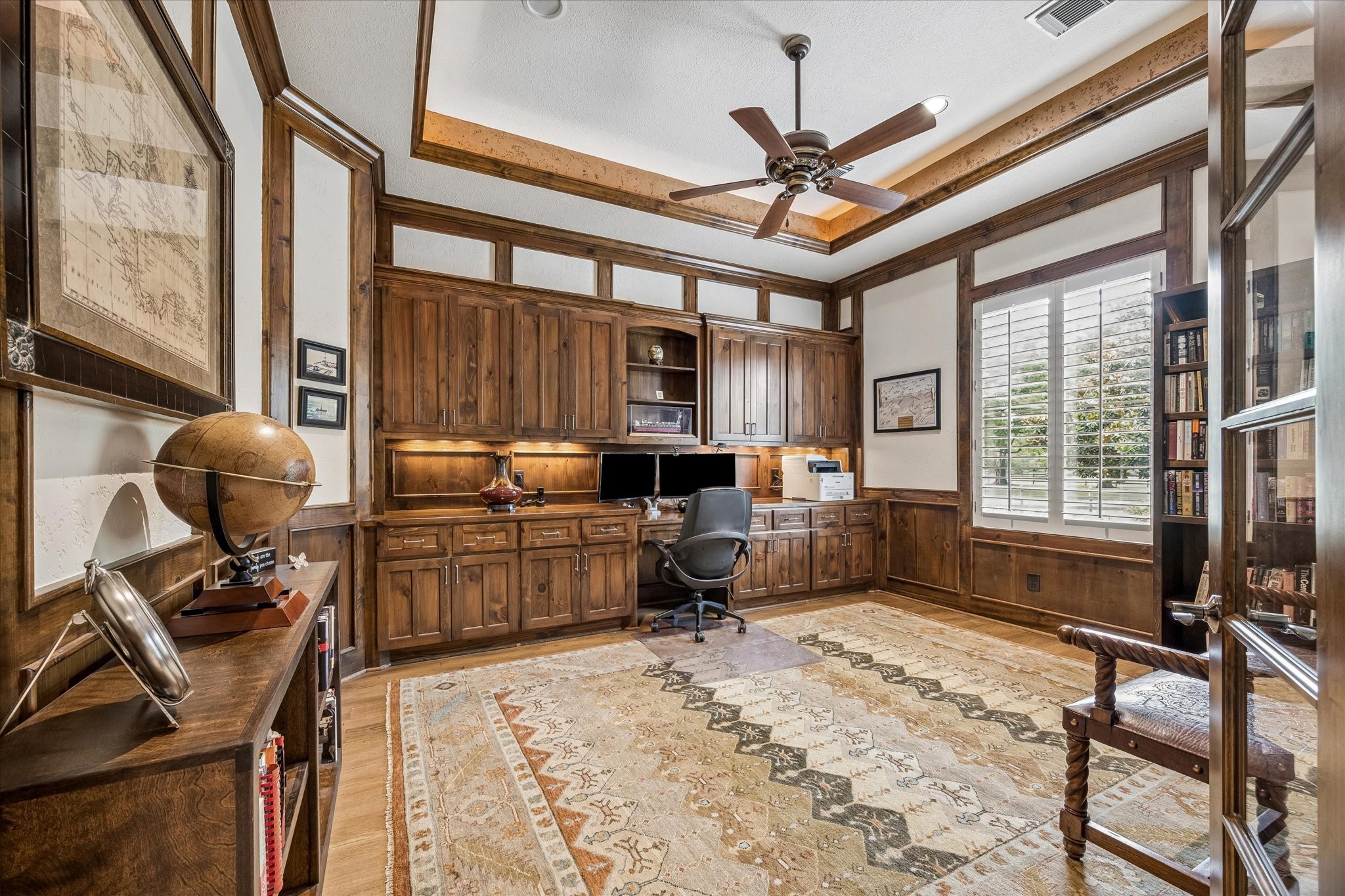 32102 Fulbrook Commons Fulshear, TX 77441 - Photo 10 of 50 Custom built-ins and extensive millwork create a distinguished study designed for productivity and inspiration. Tray lighting, glass double doors, and beautiful windows with plantation shutters are more features in this spacious private home office.
