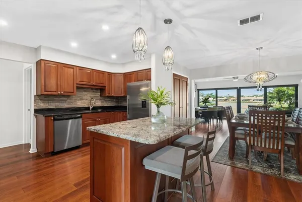 a kitchen with stainless steel appliances granite countertop a stove top oven a sink a dining table and chairs with wooden floor