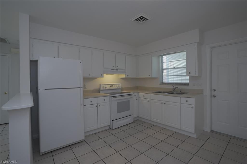 1195 South Alhambra Circle Naples, FL 34103 - Photo 9 of 34 a kitchen with granite countertop white cabinets and white stainless steel appliances