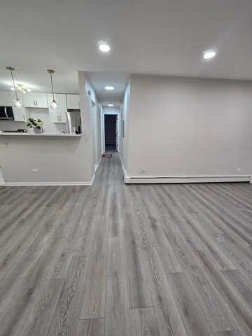 a view of an empty room and kitchen with wooden floor