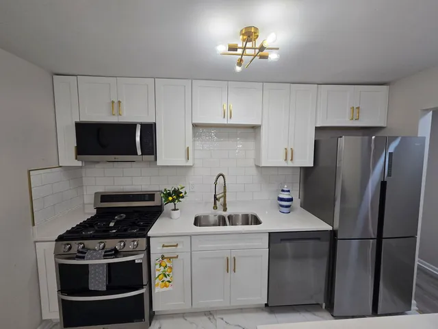 a kitchen with stainless steel appliances a stove a refrigerator a sink a stove and white cabinets