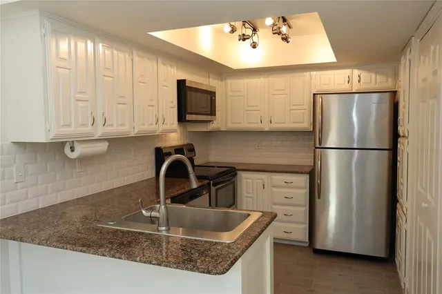 a kitchen with stainless steel appliances granite countertop a refrigerator a microwave a sink and white cabinets